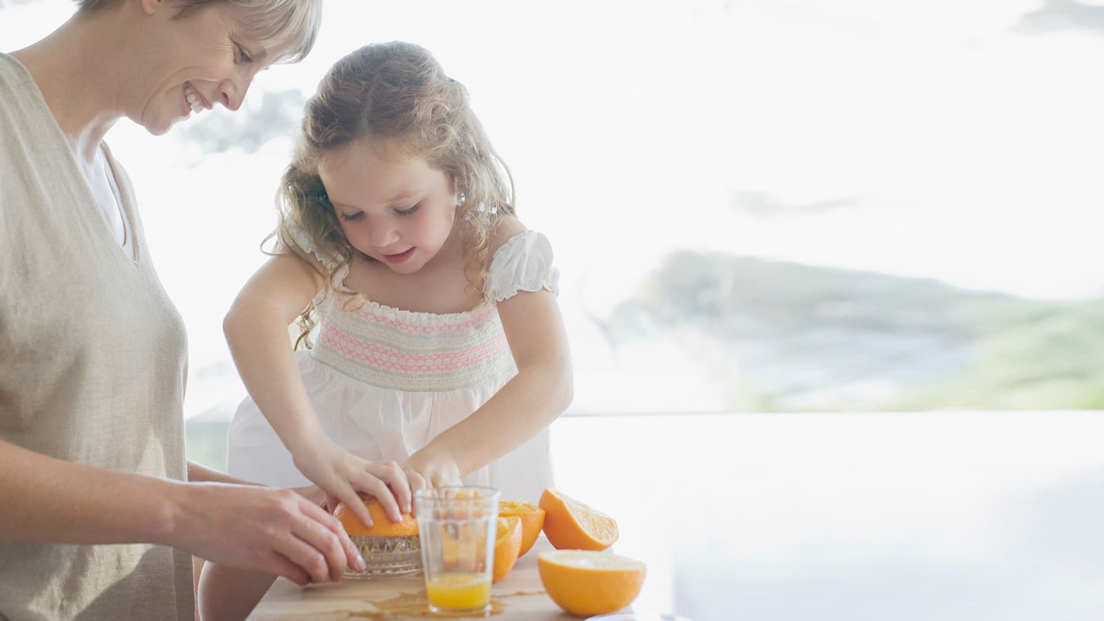 Madre e hija preparando zumo de naranja en casa